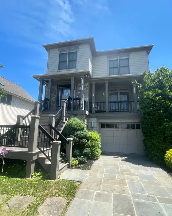 Two-story home exterior painted in sage with stone accents and black railings